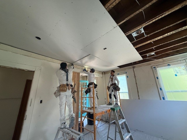 workmen holding up sheetrock and screwing it into place