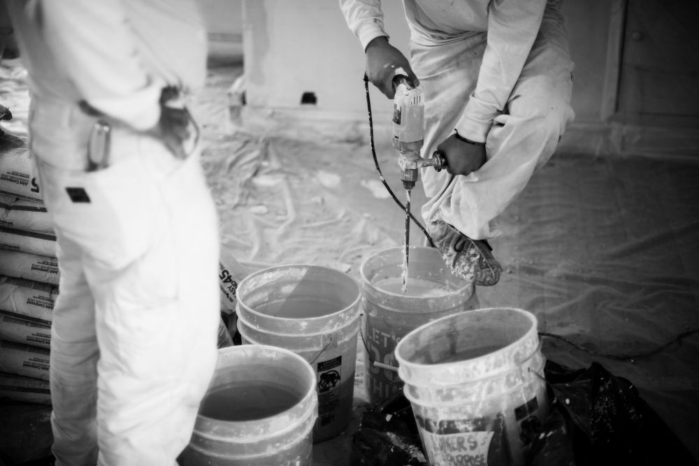 black and white shot of workmen mixing drywall mud with buckets Denver CO